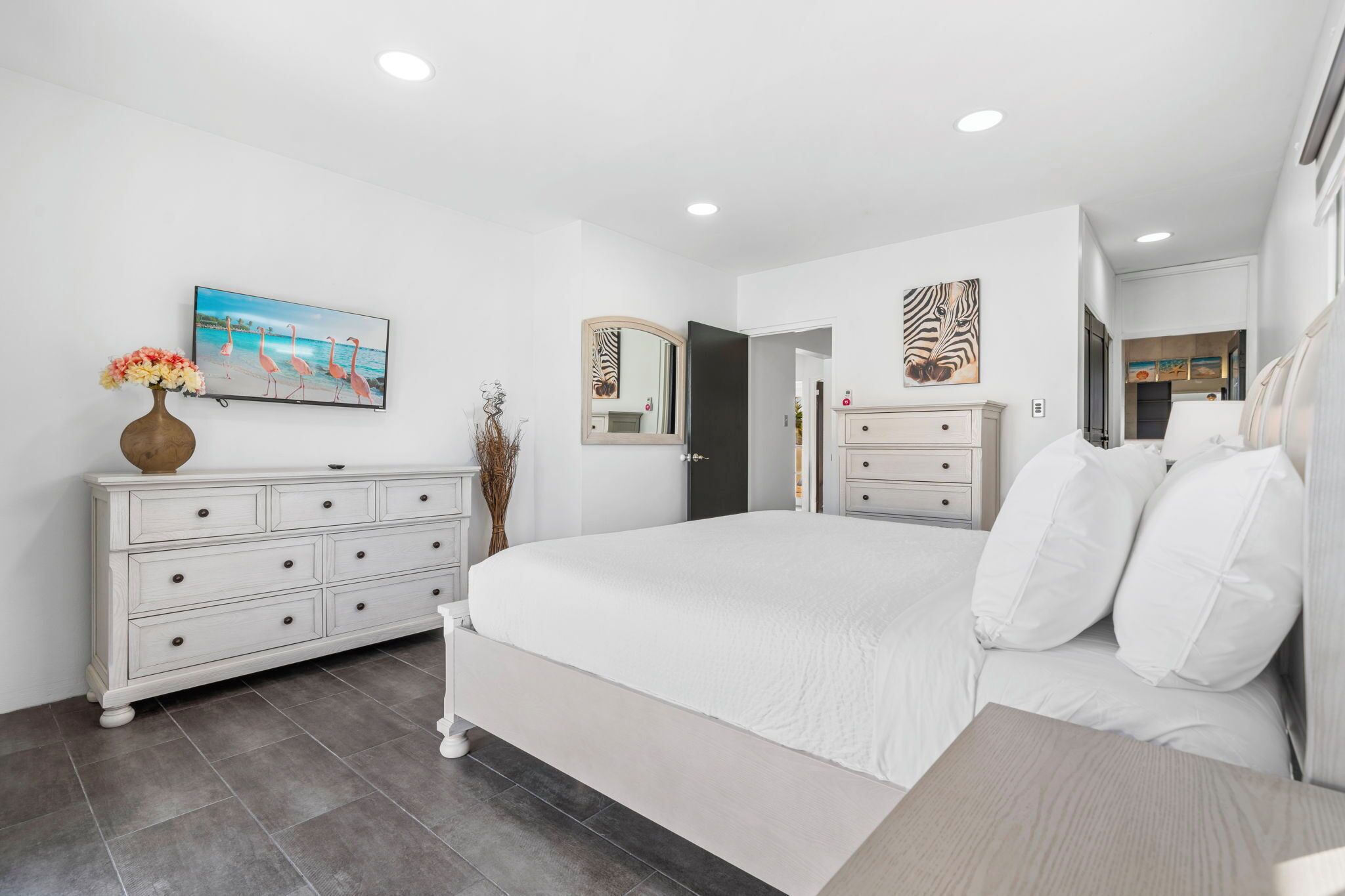 Un dormitorio moderno con una cama grande, un aparador, un espejo y un cuadro de flamencos.