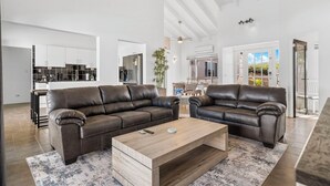 Een ruime woonkamer met twee leren banken, een houten salontafel en een keuken op de achtergrond.