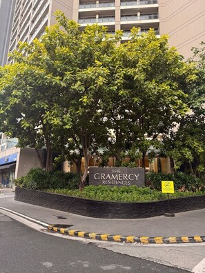 Le Gramercy Residences, reconnaissable à son panneau indicateur, est entouré d’une végétation luxuriante et d’un mur de briques.