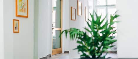 Un couloir orné de tableaux encadrés aux murs, une porte donnant sur une autre pièce et une plante en pot au premier plan.