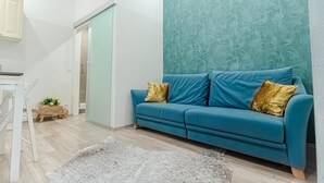 Un salón moderno con un sofá azul verdoso, una silla blanca, una mesita de madera con flores y una alfombra gris.