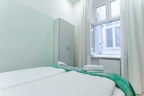 Un dormitorio con cama, armario, ventana con cortinas y radiador.