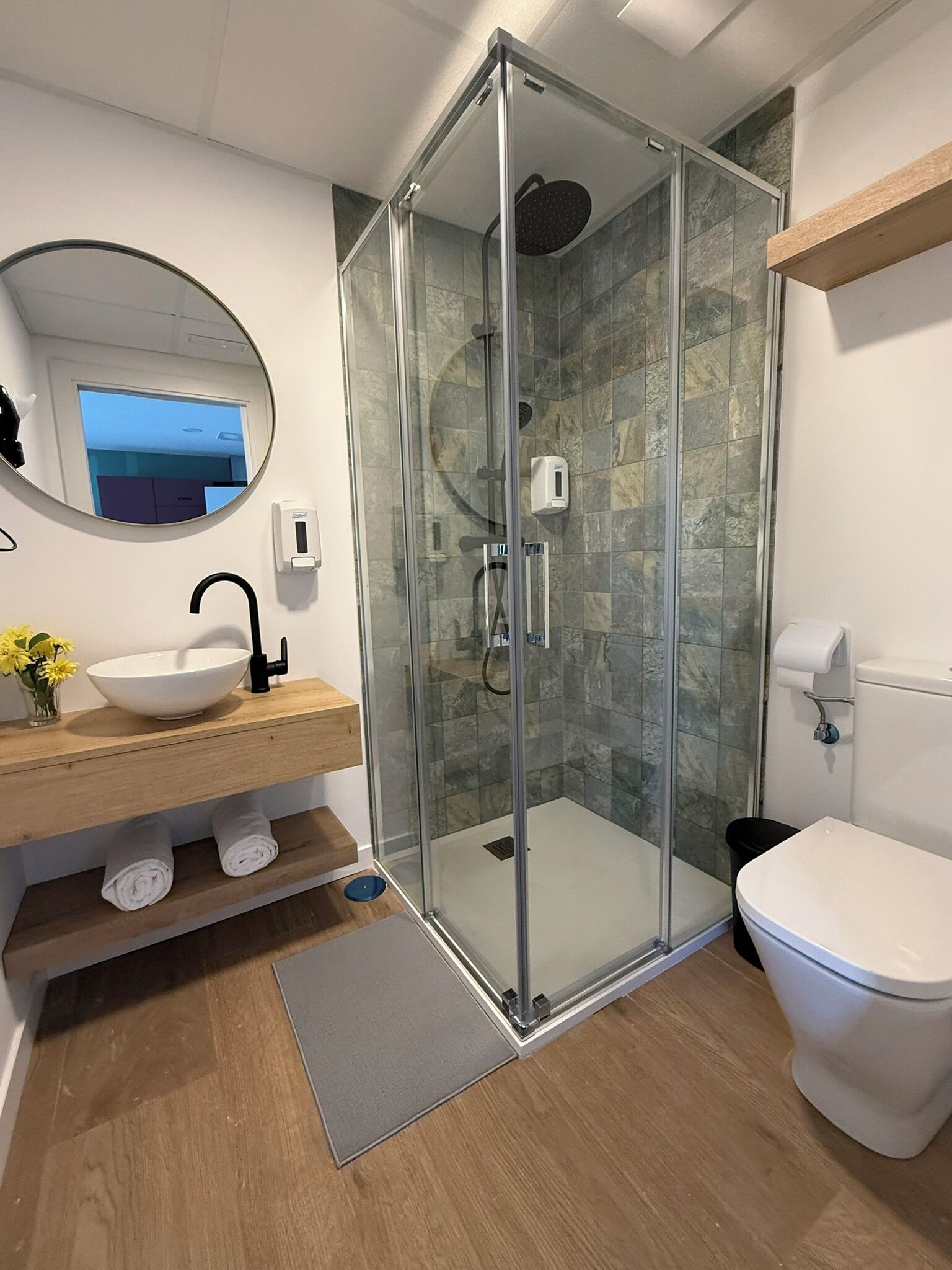 Un bagno moderno con cabina doccia in vetro, lavandino bianco e water.
