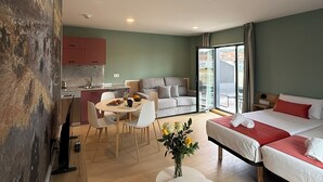 Une chambre d’hôtel moderne dotée d’un coin repas, d’une kitchenette et d’un grand lit avec une literie rouge.
