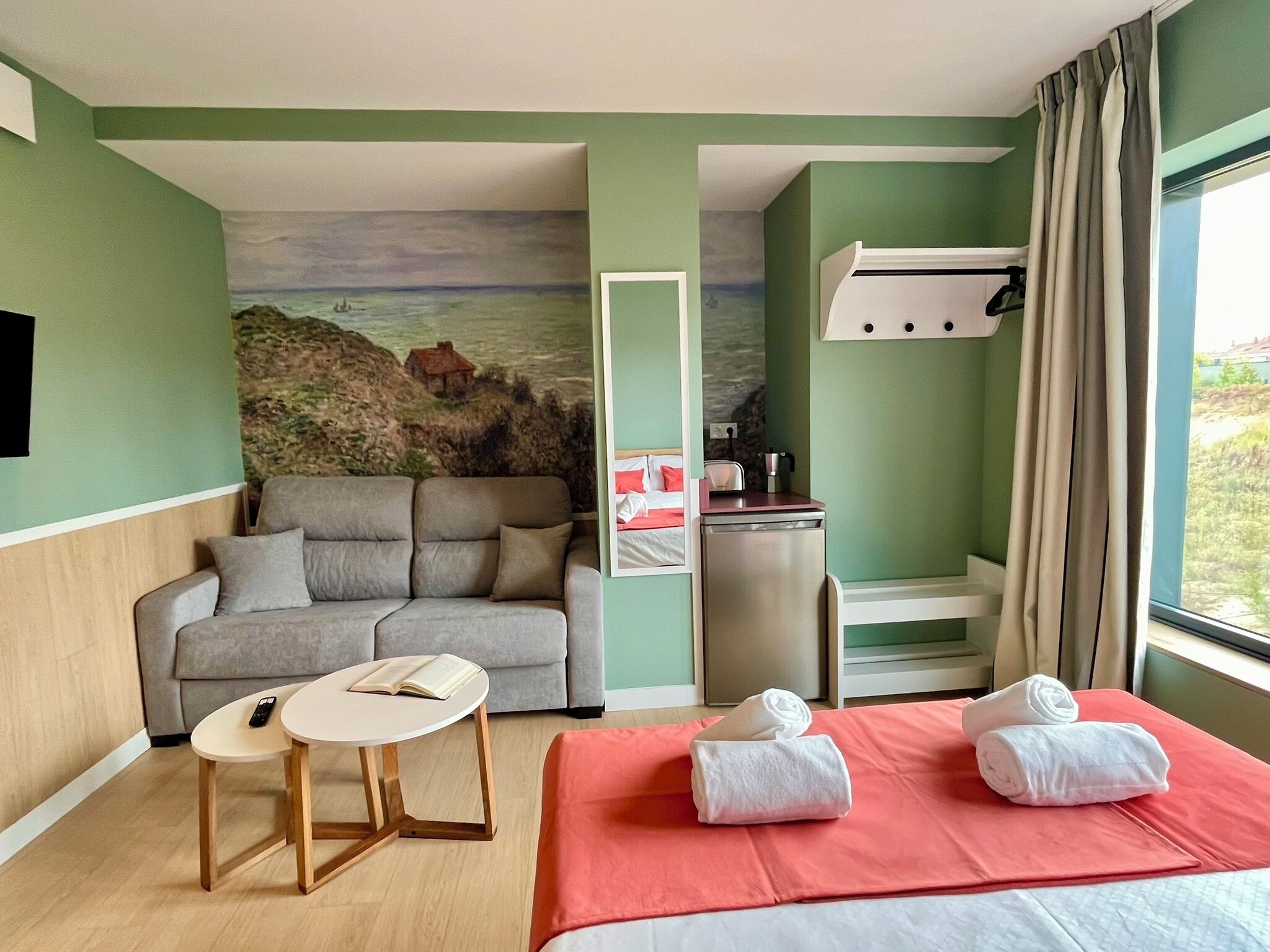 Une chambre d’hôtel avec un lit, un canapé, une petite table, un tableau au mur et une fenêtre avec des rideaux.