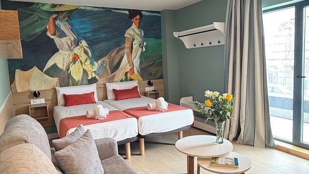 Une chambre d’hôtel moderne avec deux lits, un canapé, une petite table et un grand tableau au mur.