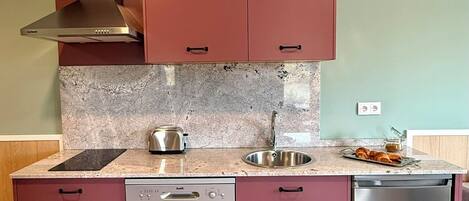 A modern kitchen with stainless steel appliances, a granite countertop, and a teal wall.