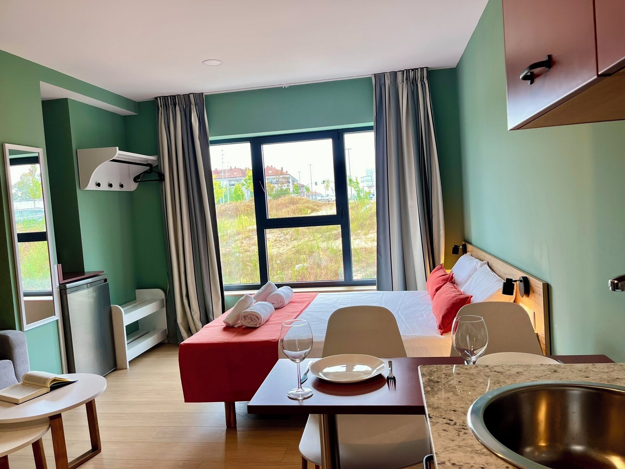 Et hotelværelse med en seng, et spisebord med stole, et tekøkken og udsigt over det fri.