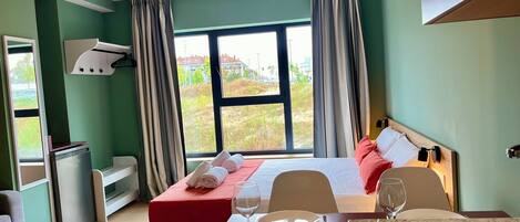 Habitación de hotel con cama, una mesa de comedor con sillas, zona de cocina y vistas al exterior.