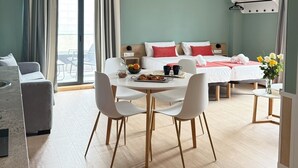 Une chambre d’hôtel moderne avec un coin repas, un lit agrémenté d’oreillers rouges et une vue dégagée sur l’extérieur grâce à une grande fenêtre.
