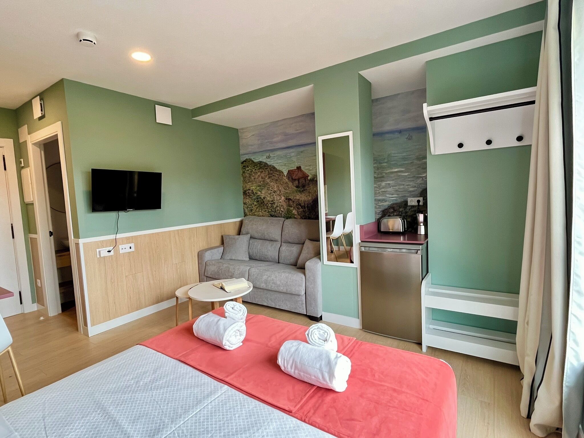Ein Hotelzimmer mit Bett, kleinem Tisch, Sofa, Küchenzeile und Fernseher.