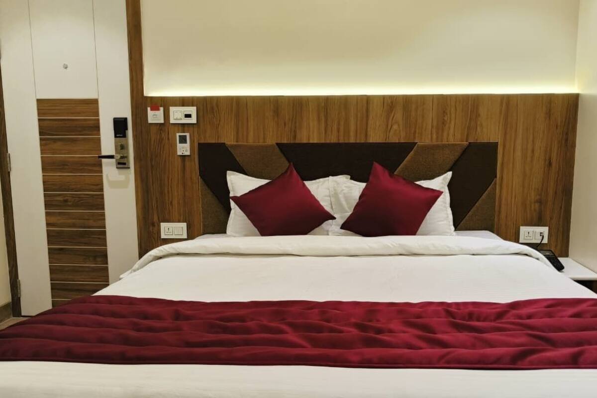 Een hotelkamer met een houten hoofdeinde, wit beddengoed en een rode plaid.