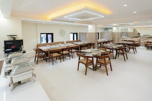 Un grand espace dédié à la salle à manger, avec plusieurs tables et chaises, un buffet et une cuisine en arrière-plan.