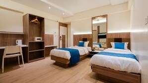 Een hotelkamer met twee bedden, een bureau, een stoel, een kledingkast en een spiegel.