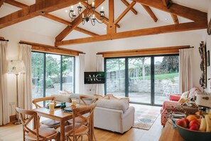 A spacious living room with a high ceiling, wooden beams, a large TV, and a dining area with a table and chairs. - New Peaceful Countryside Annex (Leyburn)