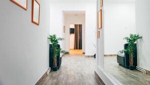 Un couloir orné de tableaux encadrés, agrémenté de plantes en pot, et d’où l’on aperçoit une autre pièce.