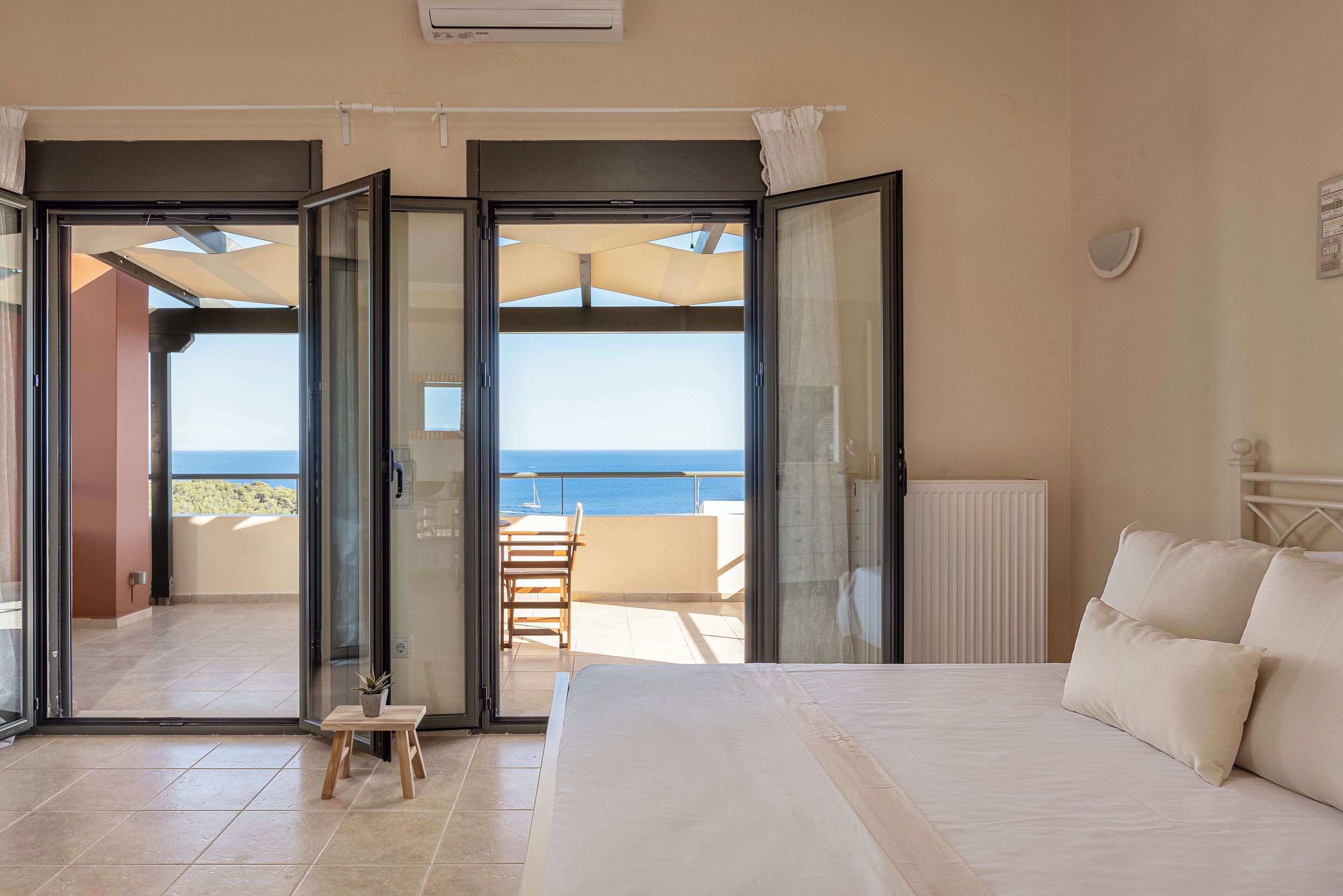 Une chambre avec un grand lit, une vue sur la mer grâce à de grandes portes coulissantes ouvertes, et une petite table avec une plante.