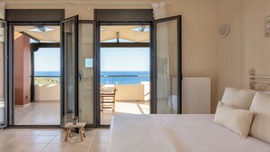 A bedroom with a large bed, a view of the sea through open sliding doors, and a small table with a plant. - Aphaias Residence Two, Aphaias Villas (Aegina)