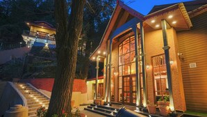 A two-story building with a staircase leading to a balcony, surrounded by trees and a well-lit entrance. - BluSalzz Terrah Hills Resort, Dalhousie-Member of SLH Hilton Hotels (Dalhousie)