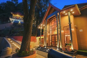 A two-story building with a staircase leading to a balcony, surrounded by trees and a well-lit entrance.