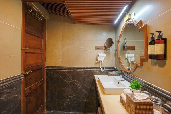 A bathroom with a wooden door, a marble wall, a sink, a mirror, and a hairdryer.