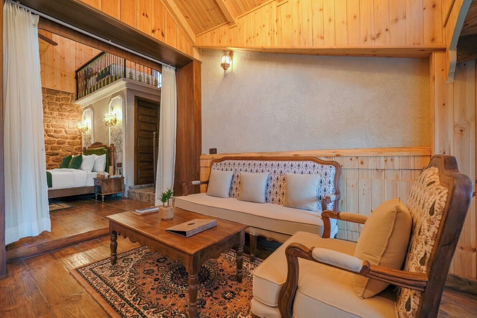 A cozy room with a wooden ceiling, a sofa with patterned cushions, a wooden coffee table, and a stone wall.