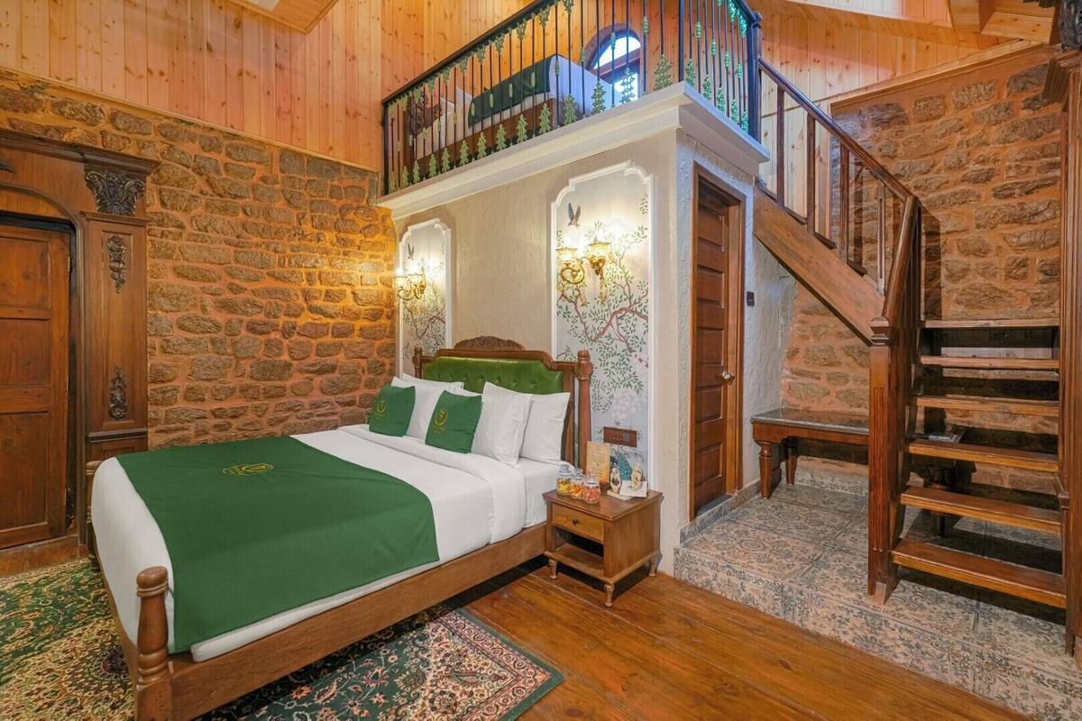 Un dormitorio con cama de madera, ropa de cama verde, una mesita de noche, un muro decorativo y una escalera.