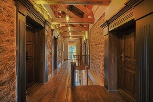 A hallway with wooden floors and stone walls, leading to a staircase.