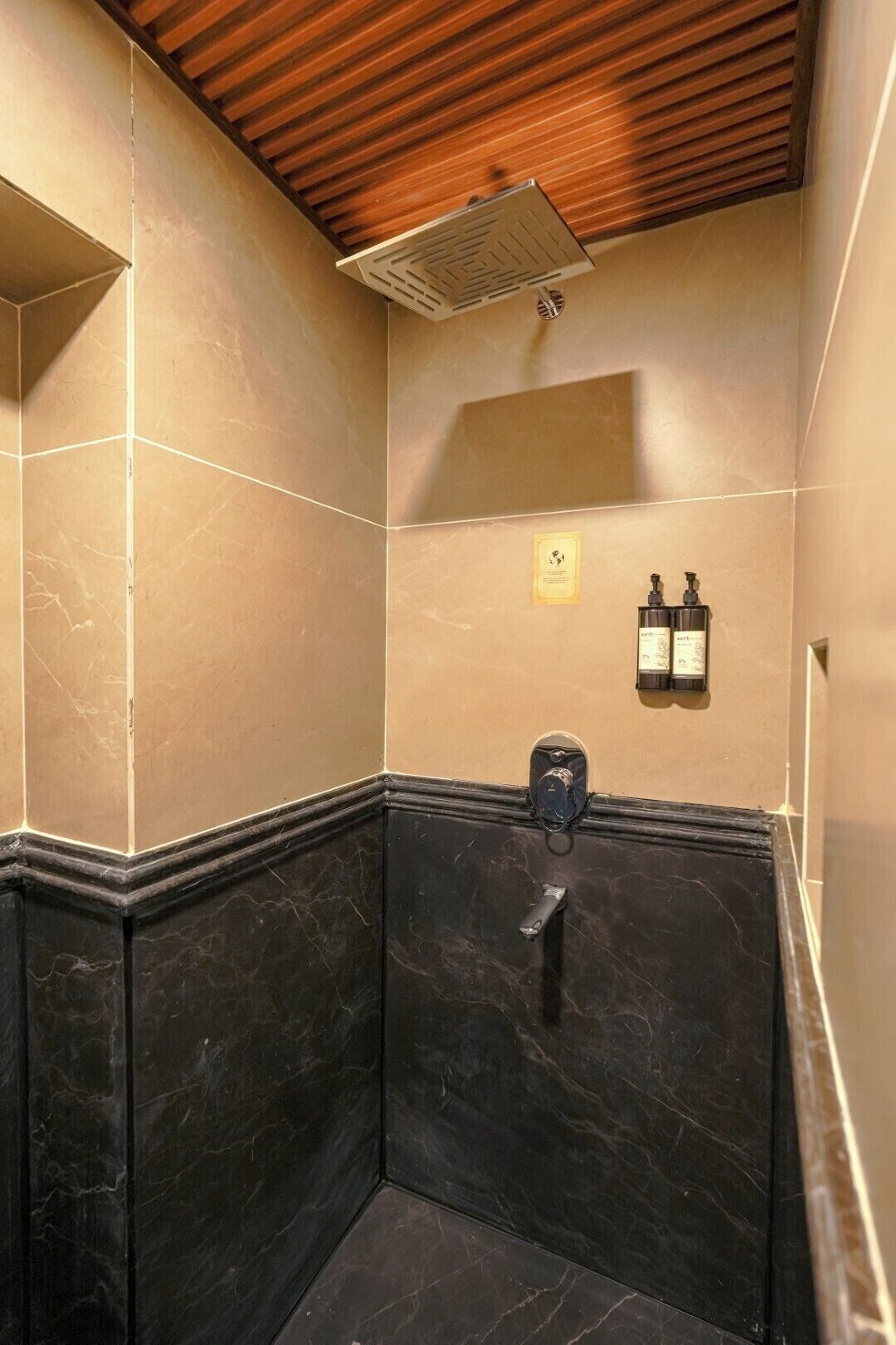 A bathroom with a shower, a hand dryer, and a soap dispenser on the wall.
