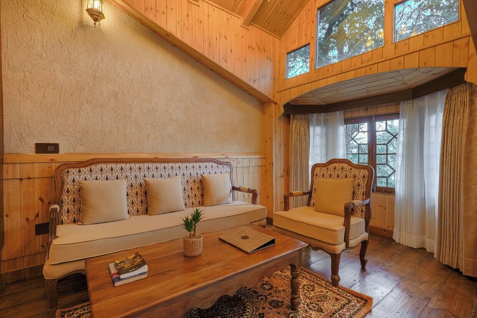 Una stanza accogliente con soffitto in legno, un divano con cuscini decorati, una poltrona e un tavolino da caffè con un libro e una pianta.