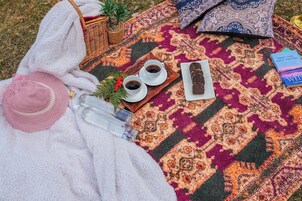 Un montaje para un picnic, con una manta, un sombrero, una bandeja con bebidas, un libro y una botella.