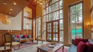 A spacious living room with large windows, a chandelier, and a mix of traditional and modern furniture. - BluSalzz Terrah Hills Resort, Dalhousie-Member of SLH Hilton Hotels (Dalhousie)