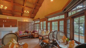 A spacious room with a wooden ceiling, large windows, a dining table set for four, and a sofa. - BluSalzz Terrah Hills Resort, Dalhousie-Member of SLH Hilton Hotels (Dalhousie)