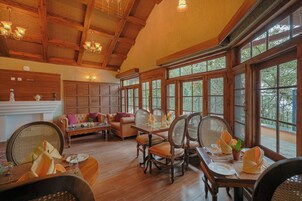 A spacious room with a wooden ceiling, large windows, a dining table set for four, and a sofa.