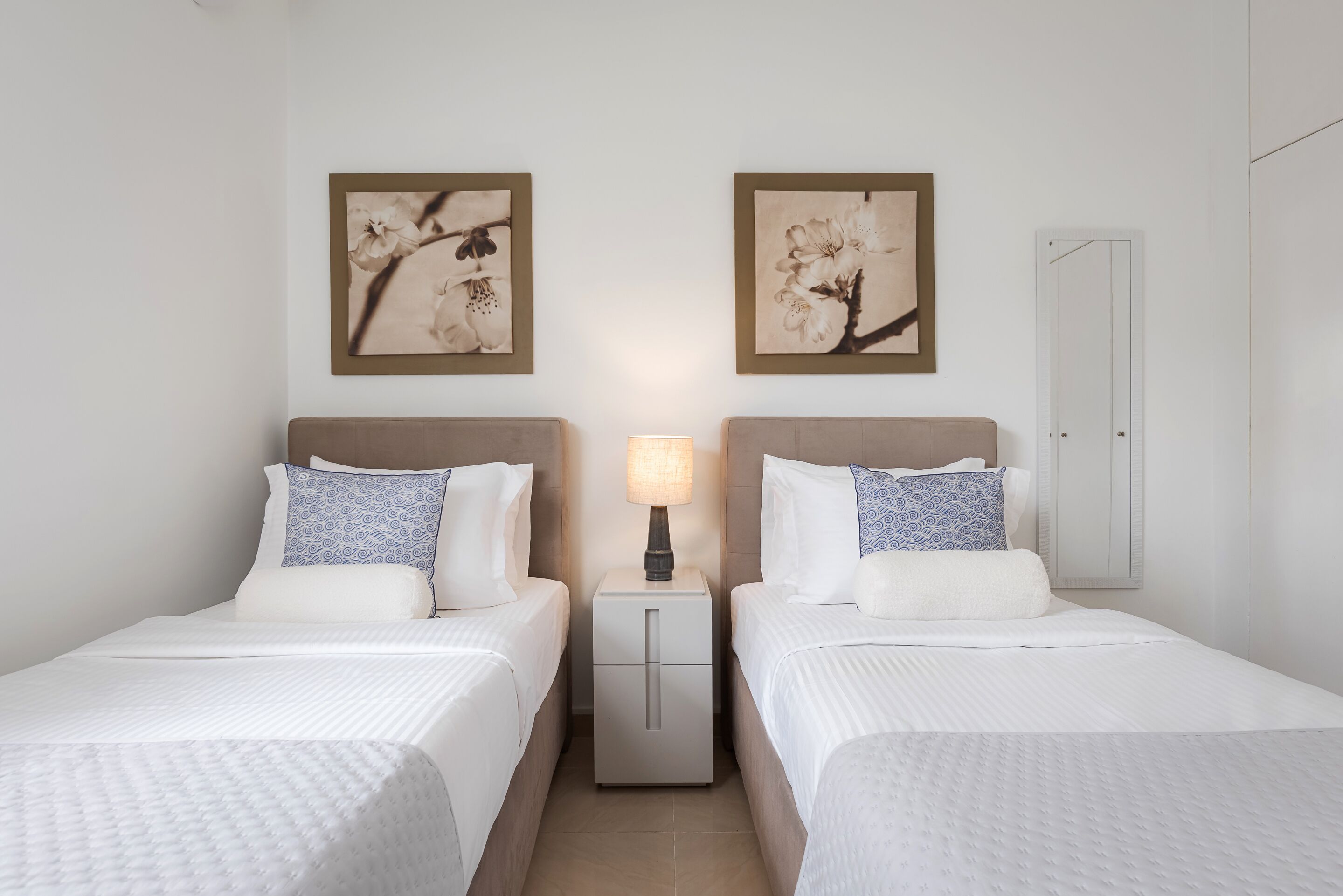 Ett hotellrum med två sängar, ett nattduksbord med en lampa och två inramade konstverk med blommotiv på väggen.