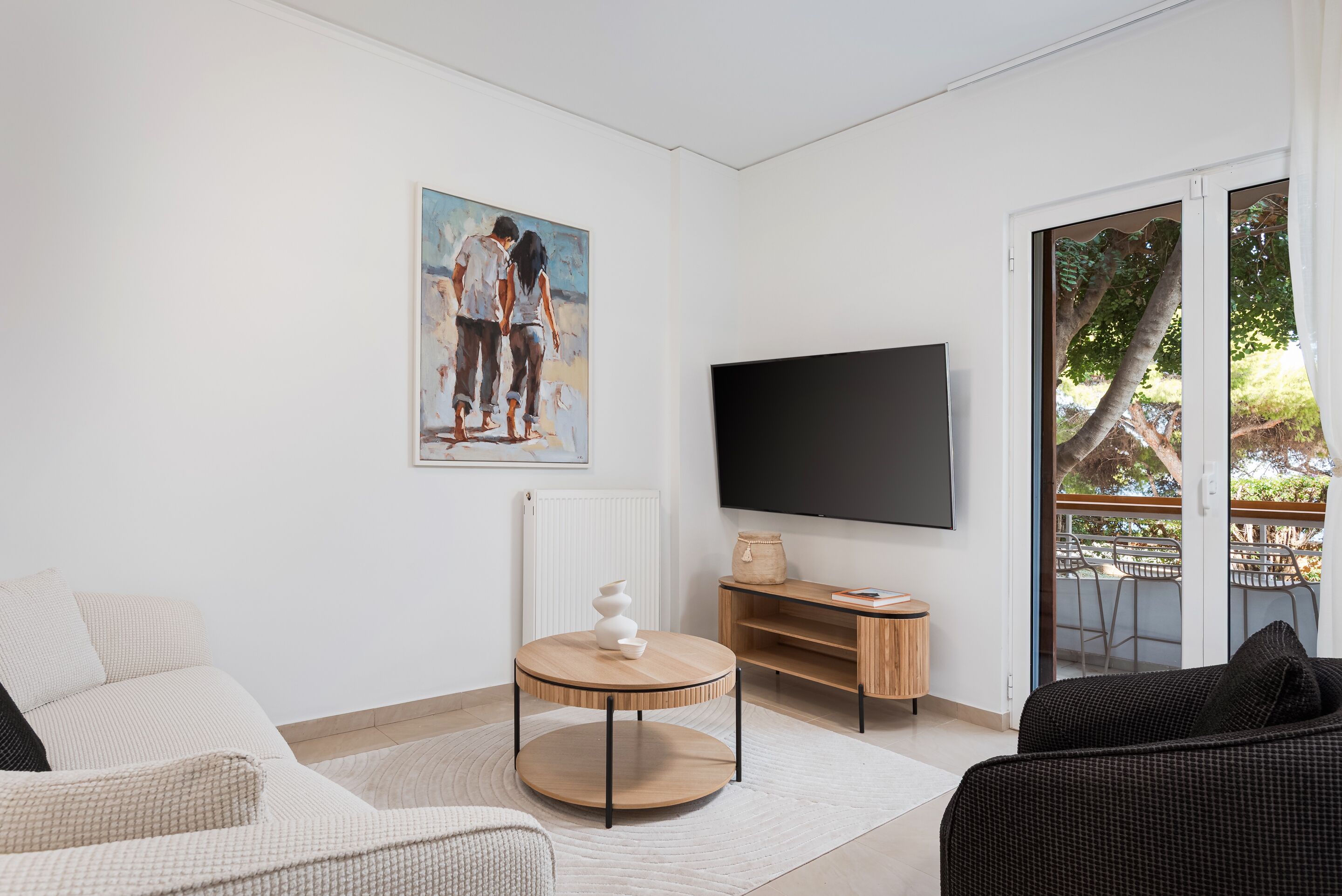 Un salon moderne avec un canapé, une table ronde en bois, un téléviseur à écran plat et un tableau accroché au mur.