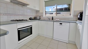 Une cuisine moderne avec des meubles blancs, une cuisinière à gaz, un four, un lave-vaisselle et une fenêtre donnant sur l’extérieur.
