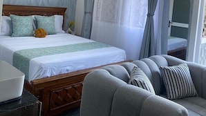 A hotel room with a bed, a sofa, a ceiling fan, and a window with curtains. - Relax & Recharge at Casa Luminosa Studio Apartment (Mtwapa)