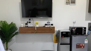 A compact living space with a flat-screen TV, a small refrigerator, a microwave, and a dining area with two round tables. - Relax & Recharge at Casa Luminosa Studio Apartment (Mtwapa)