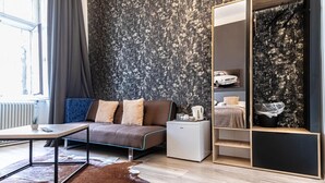 Ein modernes Zimmer mit Sofa, Couchtisch, kleinem Kühlschrank und Kleiderschrank mit Spiegel.