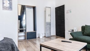 Ein modernes Zimmer mit Bett, Tisch, grünem Sofa, Spiegel und Kleiderschrank.
