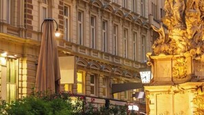 Fachada de um edifício clássico com uma grande estátua dourada em primeiro plano.