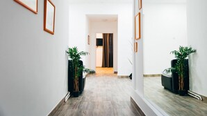 Um corredor com quadros nas paredes, plantas em vasos e vista para outro quarto.