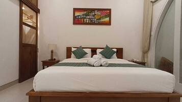 A neatly made bed with white linens and green striped pillows, a wooden headboard, and a painting on the wall.