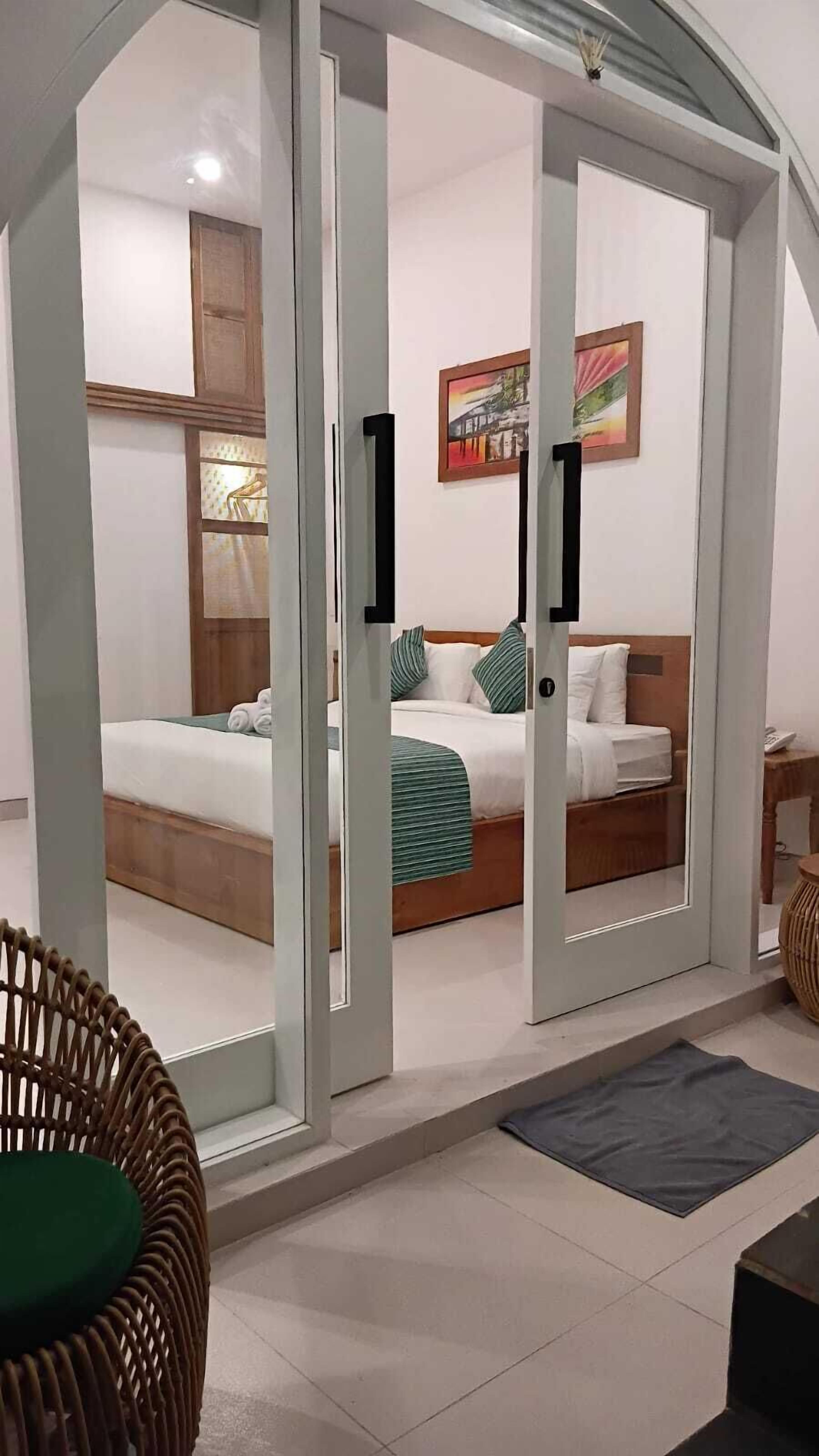 A hotel room with a bed, a chair, a painting, and a window.