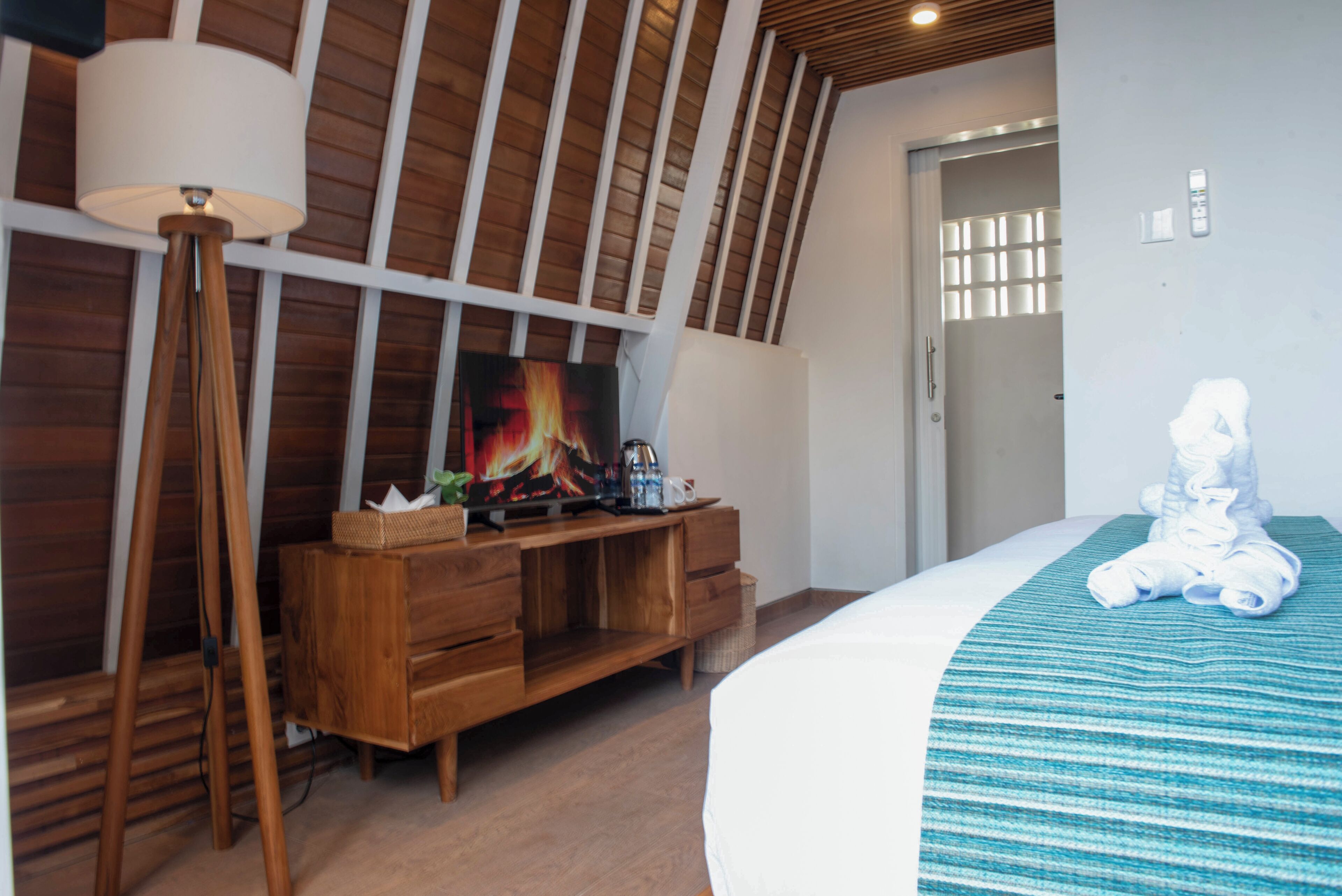 Une chambre avec un plancher en bois, un lit recouvert d’une couverture à rayures, une commode en bois, une lampe et un tableau accroché au mur.