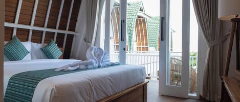 Habitación de hotel con una cama grande, cabecera de madera, balcón con vista a un edificio y una lámpara en una mesita de noche.
