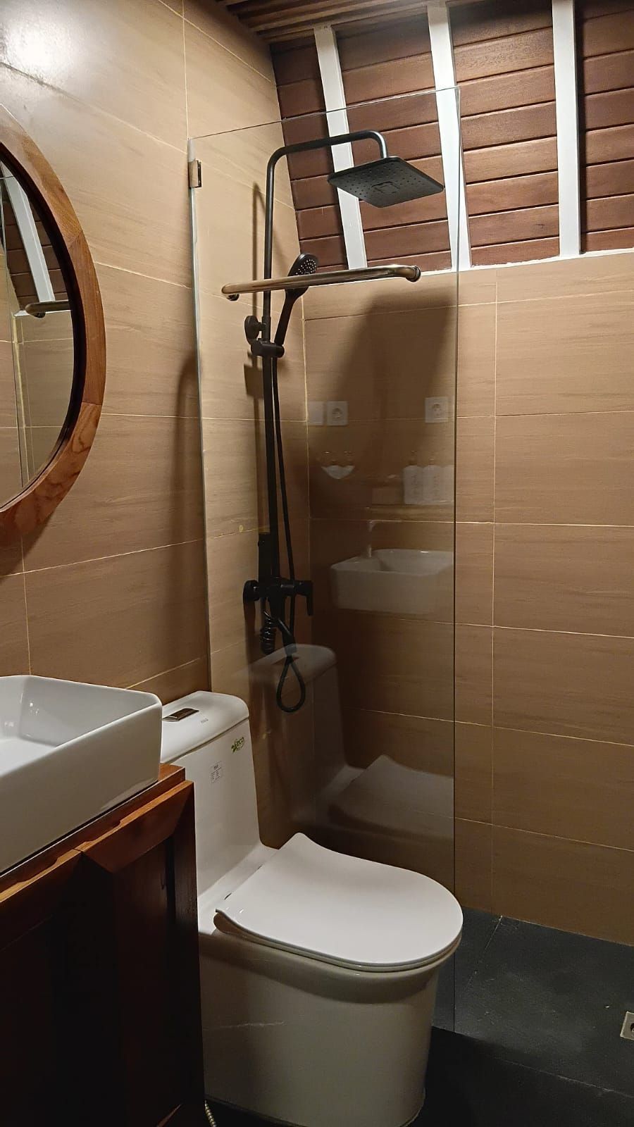 A bathroom with a toilet, a sink, a shower with a glass enclosure, and a wooden ceiling.