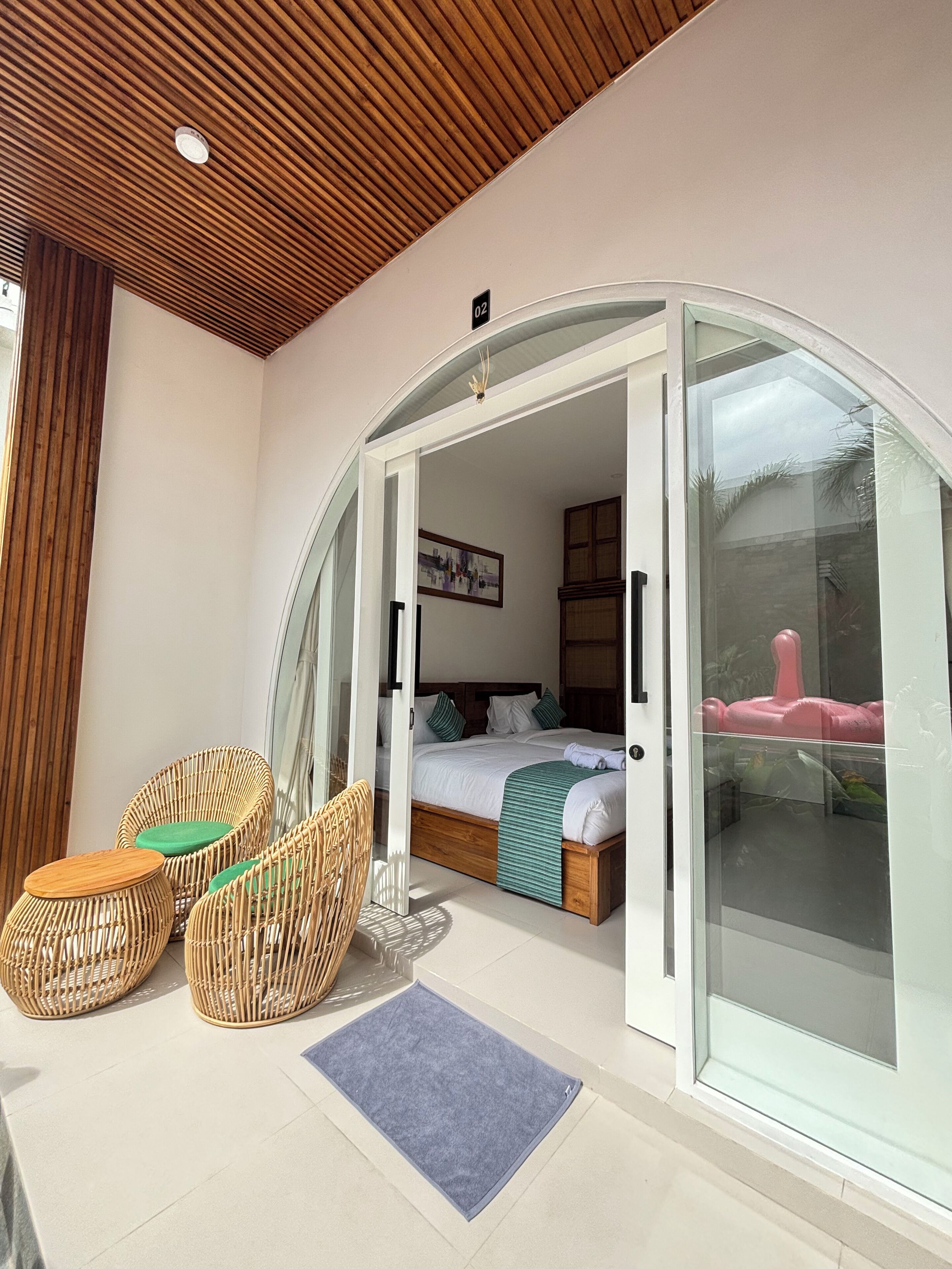A modern room with a glass door leading to a balcony, wicker furniture, a bed with a green blanket, and a framed picture on the wall.
