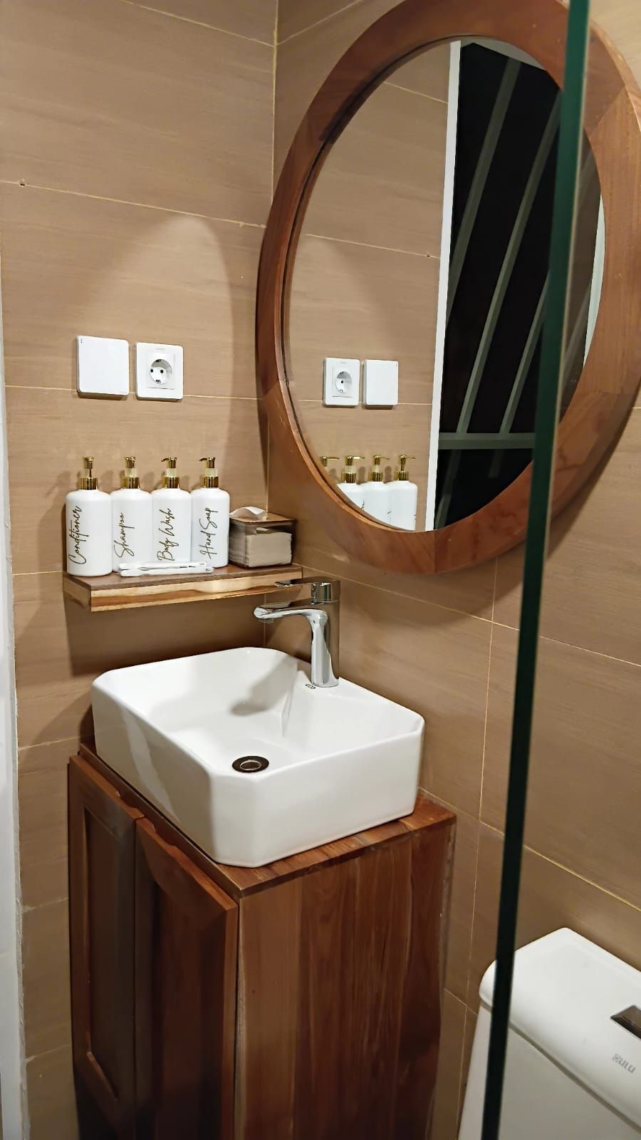 A bathroom with a white sink, wooden vanity, and a round mirror.